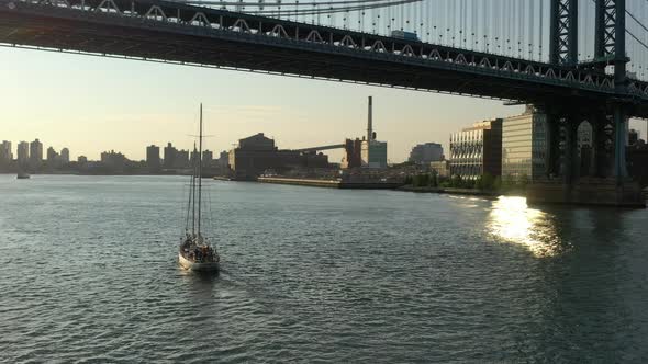 A low angle view over the East River at sunrise. The camera dolly in and pan right behind a sailboat