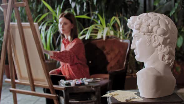 Artist in an Art Studio with Plants Young Pretty Woman Drawing a Greek Head Sculpture on a
