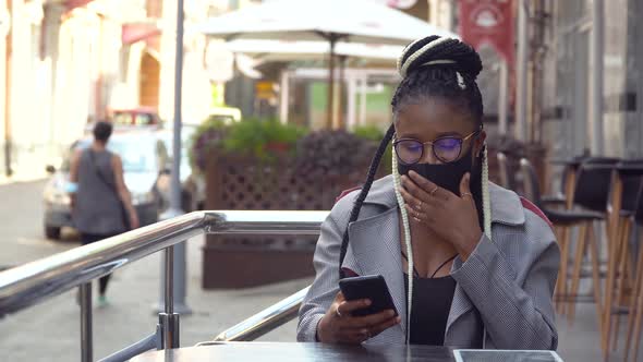 African American Girl in Mask Chatting with Friends and Drinking Coffee in Street Cafe