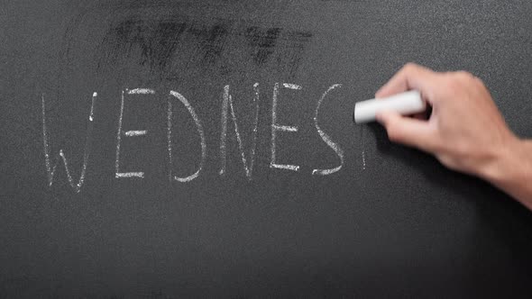 Hand writing word Wednesday on blackboard with chalk.