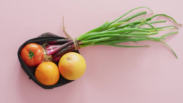 Video of fresh fruit and vegetables in black bag over pink background