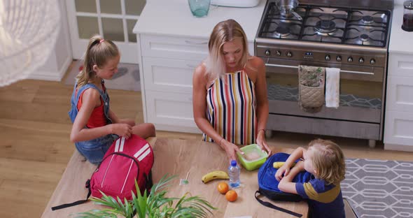 Caucasian mother in kitchen preparing packed lunches and talking with son and daughter