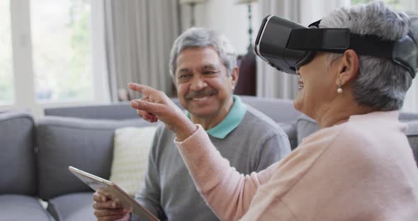 Happy mixed race senior couple wearing vr headset and having fun at home