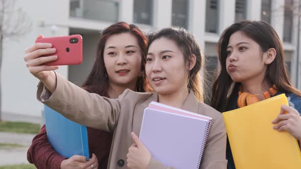 Asian college students taking a selfie with a mobile phone while standing outside the university