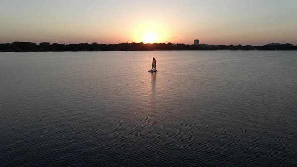 sailboat in the middle of the lake with the sun setting down in the horizon