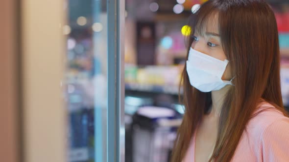 Asian woman wearing face mask and holding shopping basket in supermarket department store.