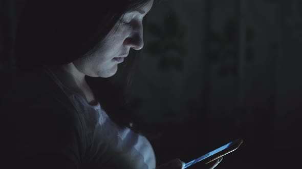 Young Woman Sitting at Night with Phone in Social Networks