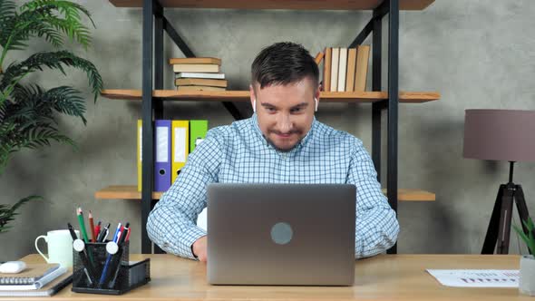 Smiling man sitting on chair at desk in home office open and start using laptop