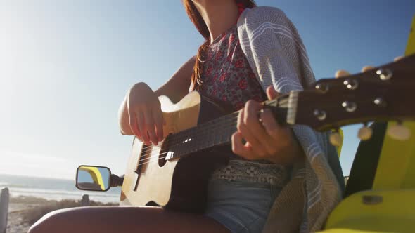 Happy caucasian woman sitting in beach buggy by the sea playing guitar