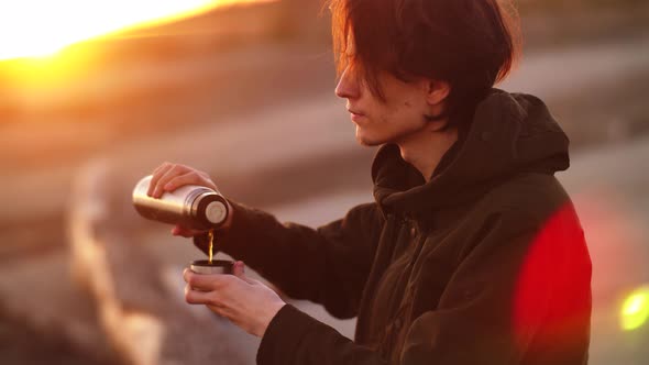 A Young Man on the Background of Sunset Pours Tea and Drinks It