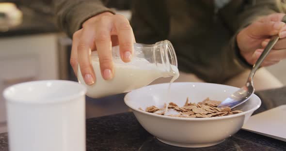 Woman in kitchen pouring milk in corn flakes 