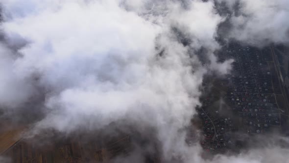 Aerial View From High Altitude of Distant City Covered with Puffy Cumulus Clouds Flying By Before