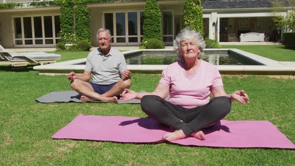 Happy caucasian senior couple practicing yoga meditating in garden in the sun