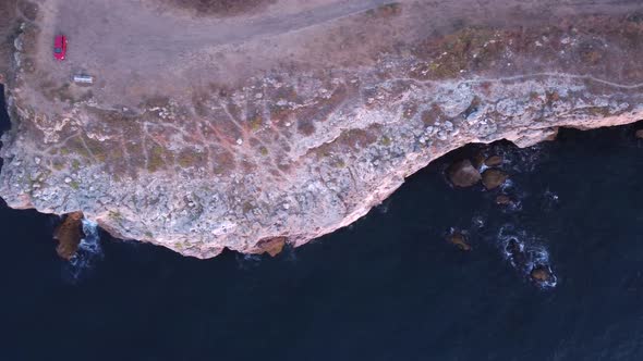 Top down aerial view of waves splash against rocky seashore, background. Flight over high cliffs of
