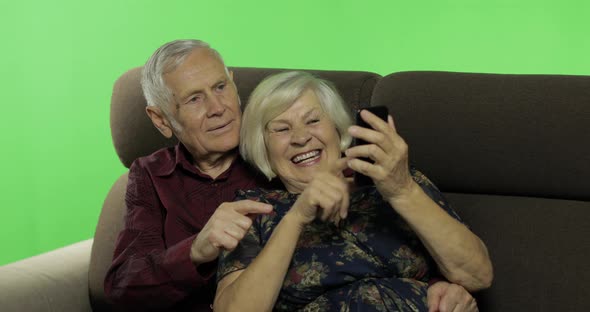 Senior Aged Man and Woman Sitting Together on a Sofa and Working on Smartphone