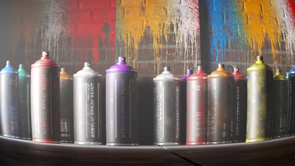 Used, colorful spray paint cans standing in front of a painted brick wall. 4KHD