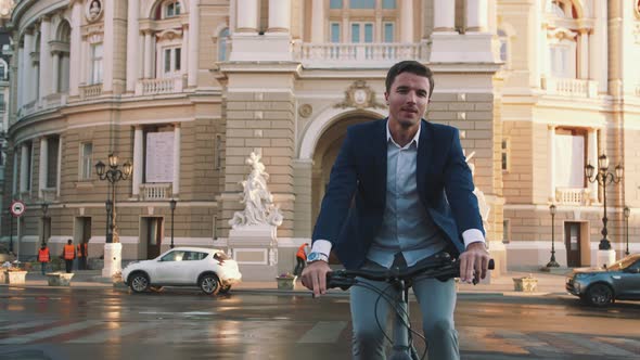 Handsome Young Man Driving His Bicycle on the Street in City Center with Architecture Background