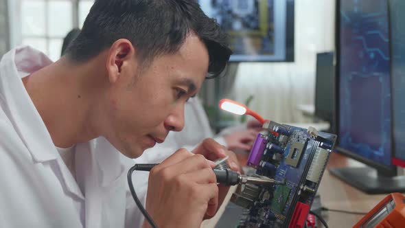 Asian Male Engineer Does Computer Motherboard Soldering. Scientists Design Industrial Pcb