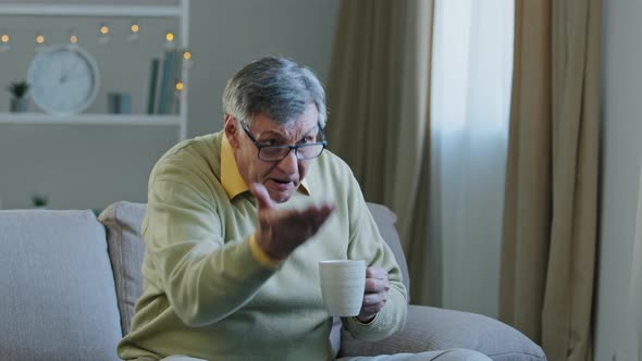 Old Elderly Mature Grandfather Man Sitting at Home Couch Watching TV Drinking Hot Tea From Cup