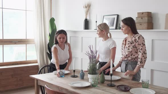 Three girls are smiling standing in the kitchen and laying out plates for a joint dinner