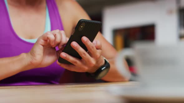 Midsection of caucasian woman using smartphone sitting at cafe in gym