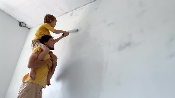 A Father and Son Both Wearing a Yellow Tshirt Paint the Wall Using a Roller Painter