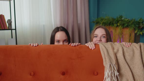 Cunning Girls Friends Siblings Playing Hide and Seek Peekaboo Game Near Sofa Looking at Camera