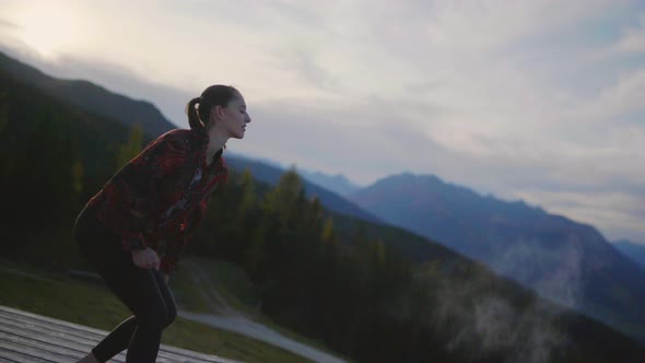 Slow motion of a young woman dancing on a wooden platform in the mountains at dusk, throwing white p