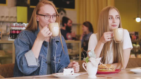 Two Young Attractive Women Have Breakfast in a Cafe. Two Friends Are Drinking Coffee