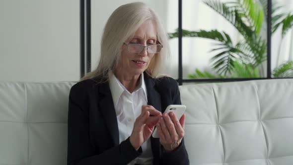 Elderly Woman Sitting on the Couch Smiling While Using Her Phone Celebrating Success