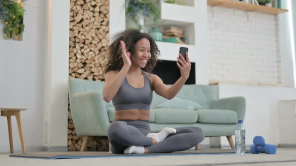 Young African Woman Talking on Video Call on Smartphone Sitting on Yoga Mat