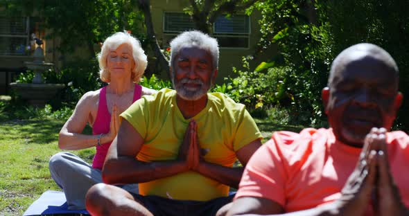 Front view of active mixed-race senior people performing yoga in the garden of nursing home 4k