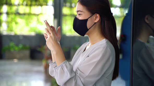 Young Beautiful Asian Woman with Surgical Mask for Face Protection Using a Phone at Office Building