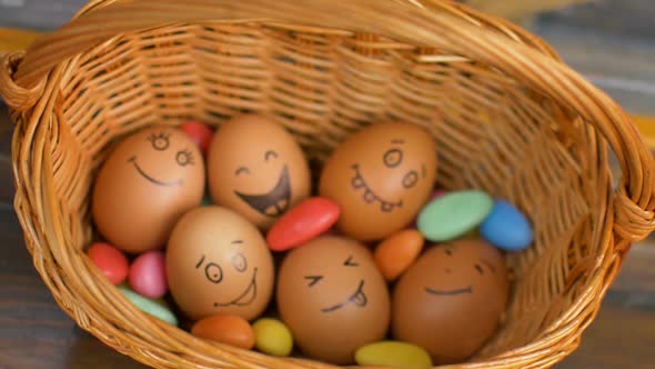 Stack of Eggs with Hand Drawn Faces on Straw Basket with Colorful Candy Easter Preparation Holiday