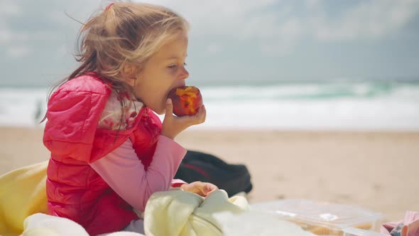 Little Girl Sits on Beach Eating Peach