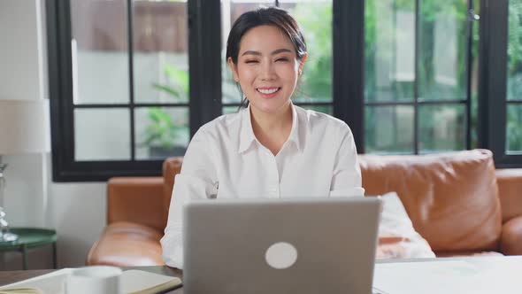 Portrait of Asian business woman working on laptop computer at home and looking at camera.