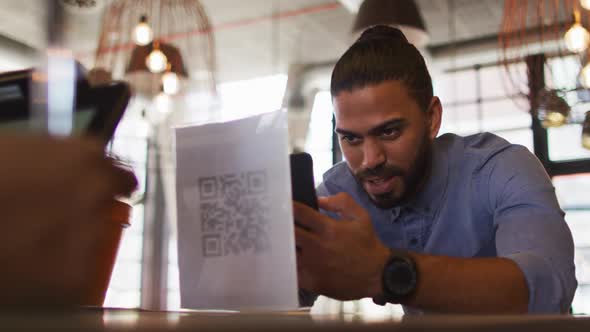 Mixed race man giving african american female cafe worker his smartphone in order to pay