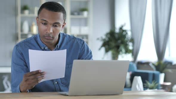 Young African Man Working on Documents and Laptop in Office