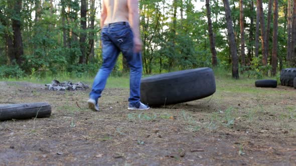 Fit muscular man doing crossfit exercises lifting big rubber tire outdoors.
