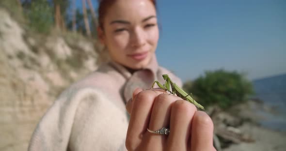 Closeup Green Mantis on Female Caucasian Hand with Blurred Young Woman Smiling at Background