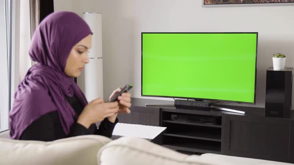 A Young Beautiful Muslim Woman Works on a Smartphone in an Apartment  TV with Green Screen