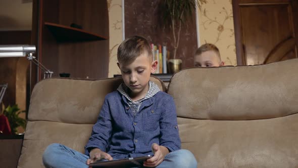 Boy Sitting on the Couch at Home and Uses Tablet PC to watch Video or Gaming