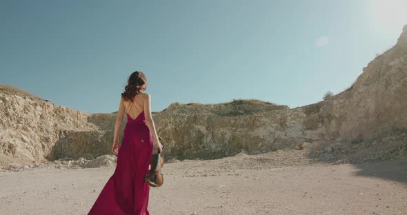 Elegant Lady Walking with Violin and Bow on Desert at Cliff Under Bright Sky