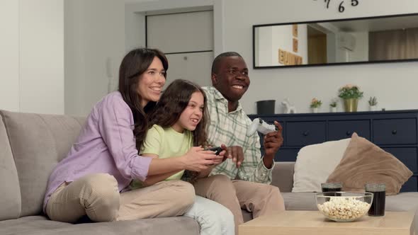 Multi Ethnic Family of Three Playing a Video Game at Home Sitting on the Couch