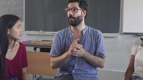 Confident Young Male Mentor Teacher Talking to Multiracial Students Teenagers Sitting in a Circle