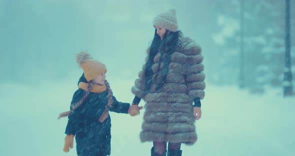 Cheerful Girl with Her Mother Walk in the Winter in the Snow