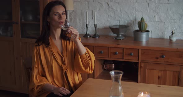 Beautiful Woman in a Yellow Blouse Drinks Water at the Table