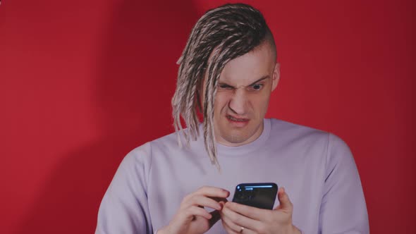Young puzzled man browsing mobile phone on red background.