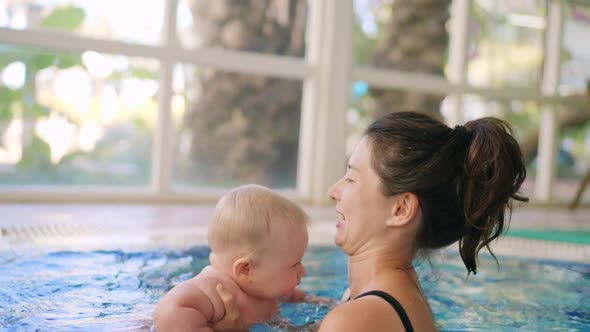 Happy Mother in Red Swimming Suit with Baby Son Surfing Water with Fun in Swimming Pool