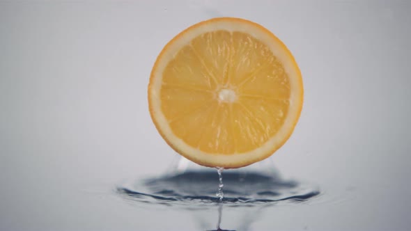 A fresh orange slice in circle shape falls down onto a surface in slow motion